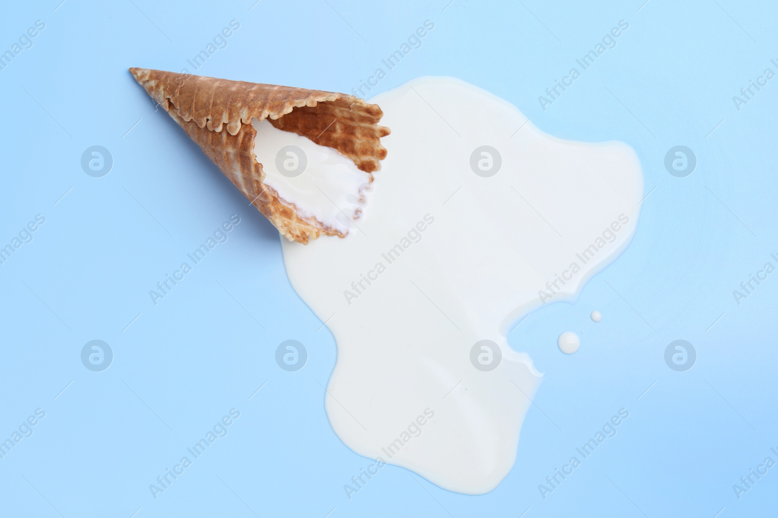 Photo of Melted ice cream and wafer cone on light blue background, top view