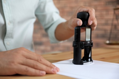 Male notary stamping document at table, closeup