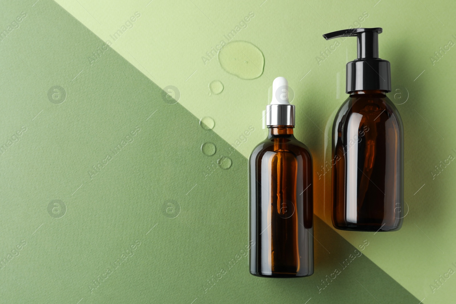 Photo of Bottles and drops of hydrophilic oil on color background, flat lay. Space for text