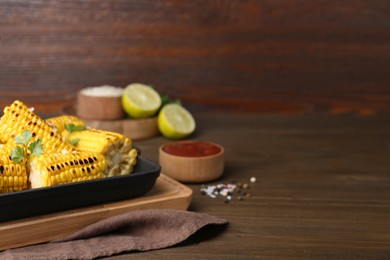 Photo of Tasty grilled corn and ingredients on wooden table. Space for text