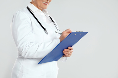 Mature doctor with clipboard on light grey background, closeup