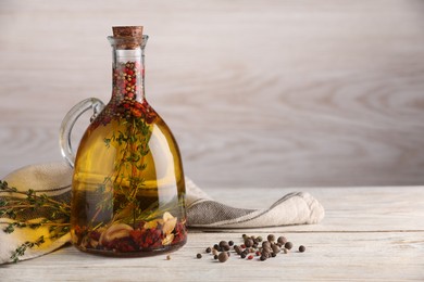 Photo of Glass jug of cooking oil with spices and herbs on white wooden table. Space for text