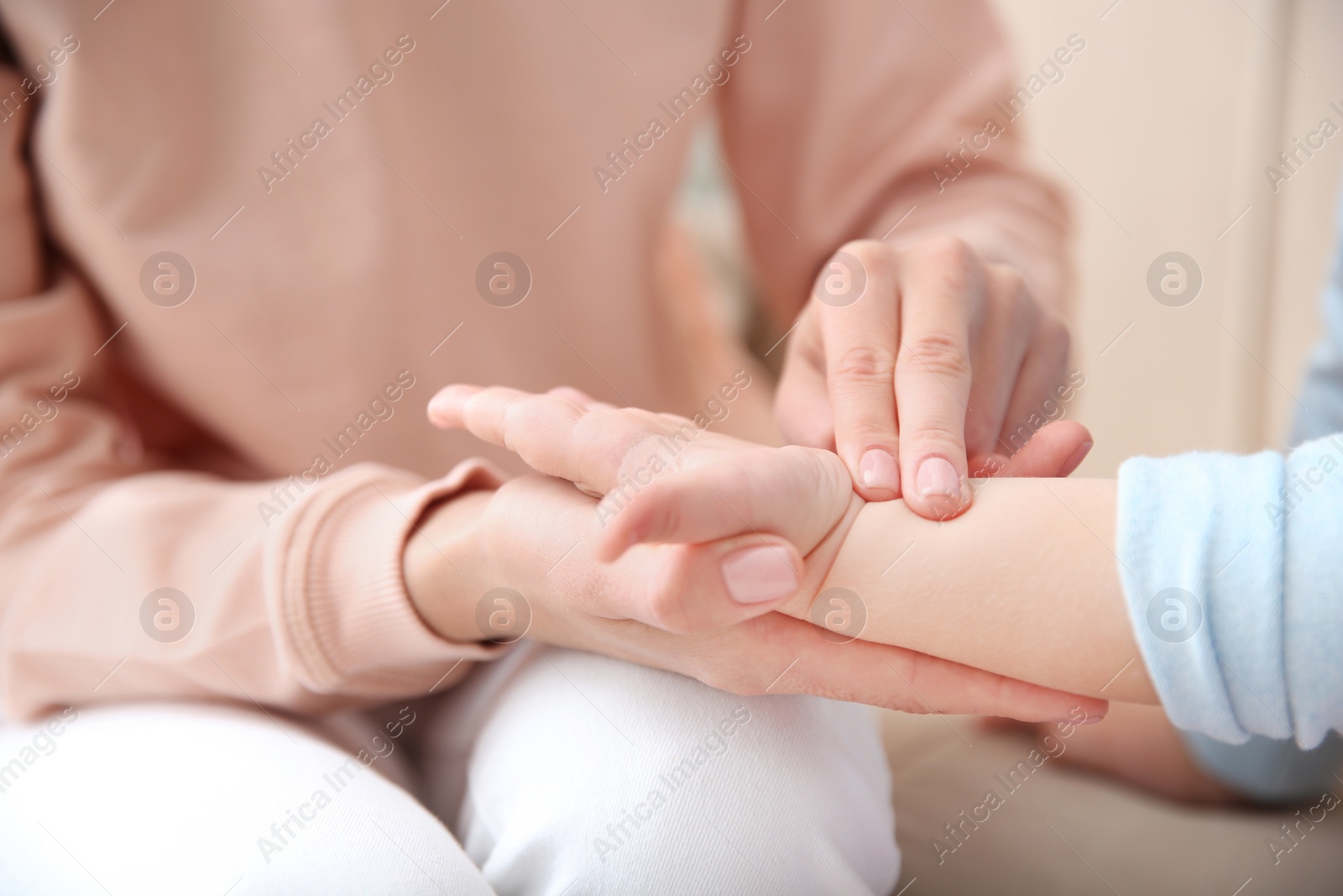 Photo of Young woman checking little girl's pulse with fingers indoors, closeup
