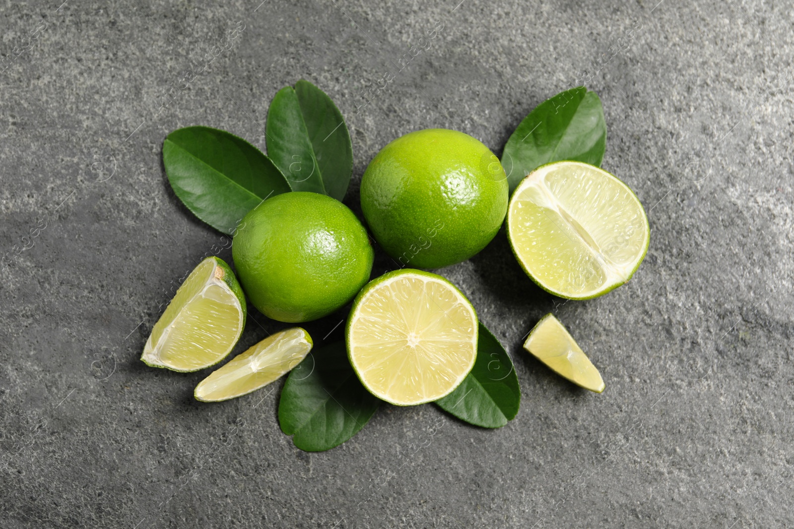 Photo of Fresh ripe limes and leaves on grey table, top view