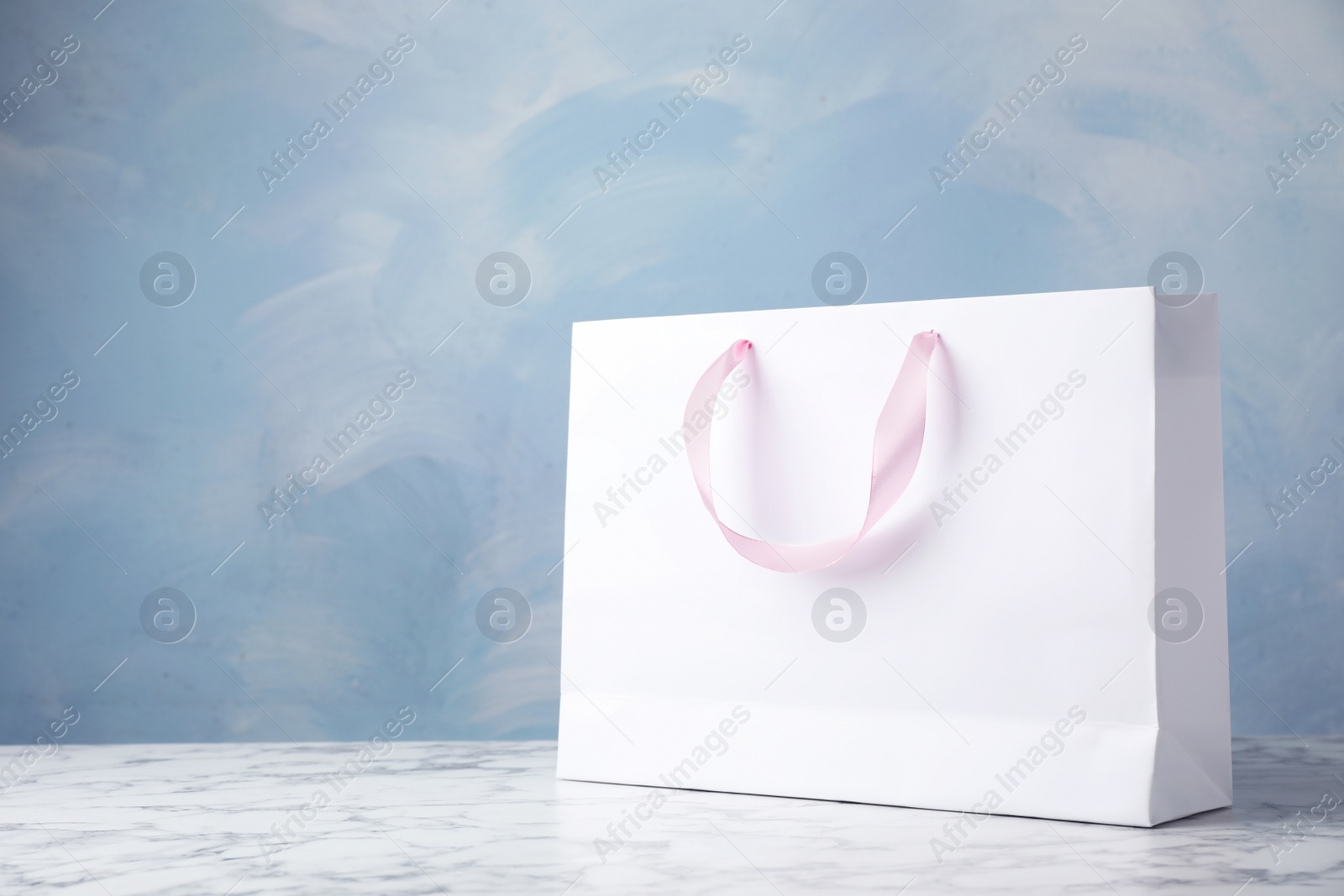 Photo of Paper shopping bag with ribbon handles on table against color background. Mockup for design