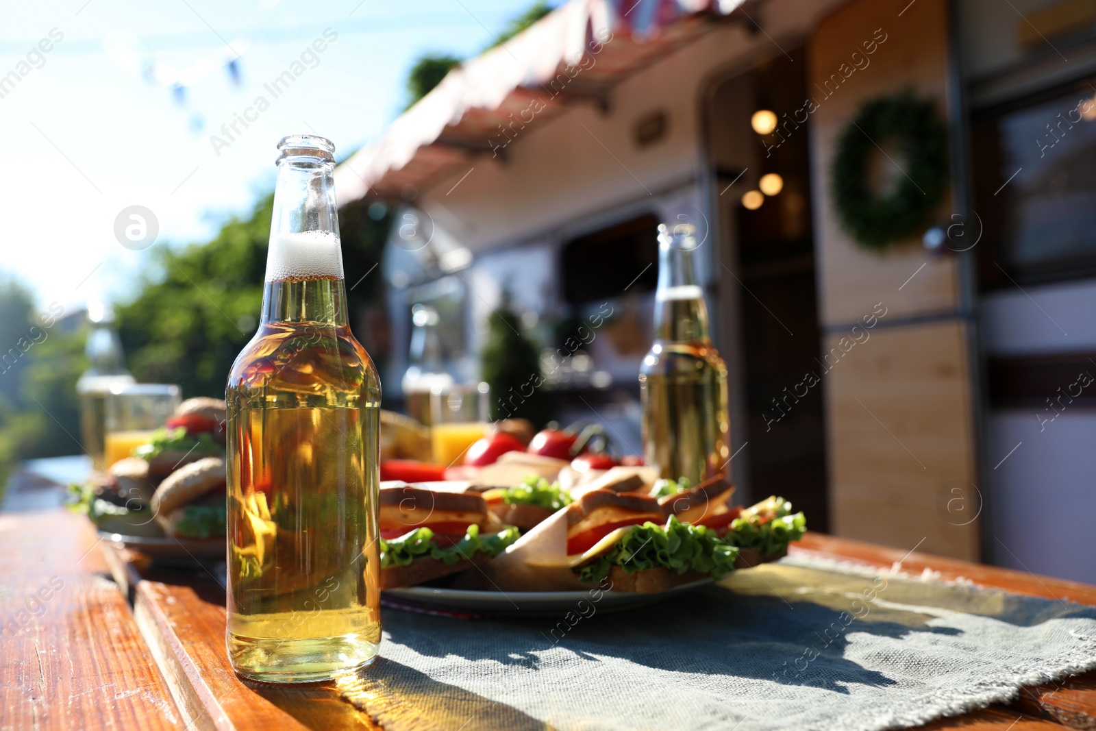 Photo of Bottles of beer and sandwiches on wooden table near motorhome. Camping season