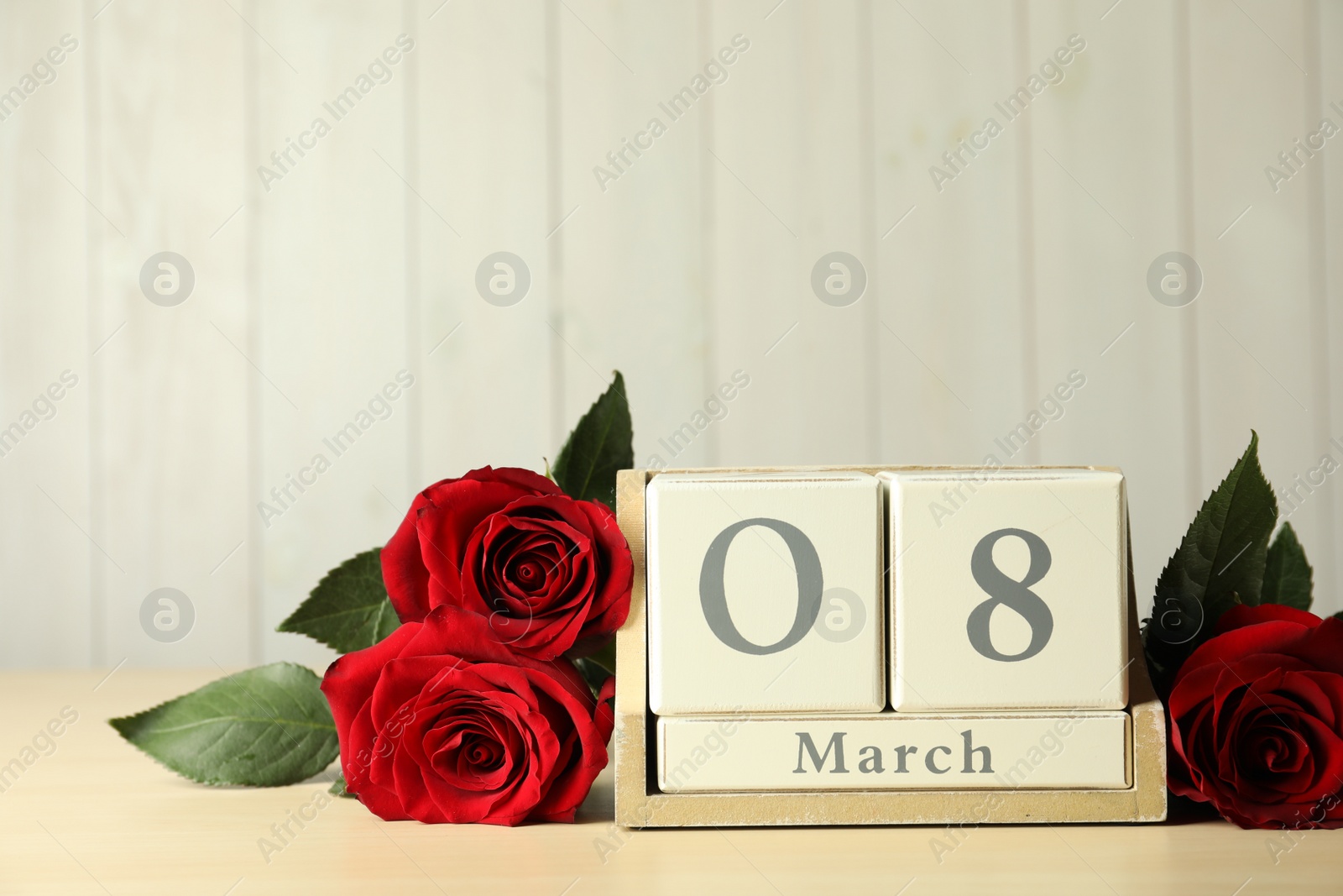 Photo of Wooden block calendar with date 8th of March and roses on table against light background, space for text. International Women's Day