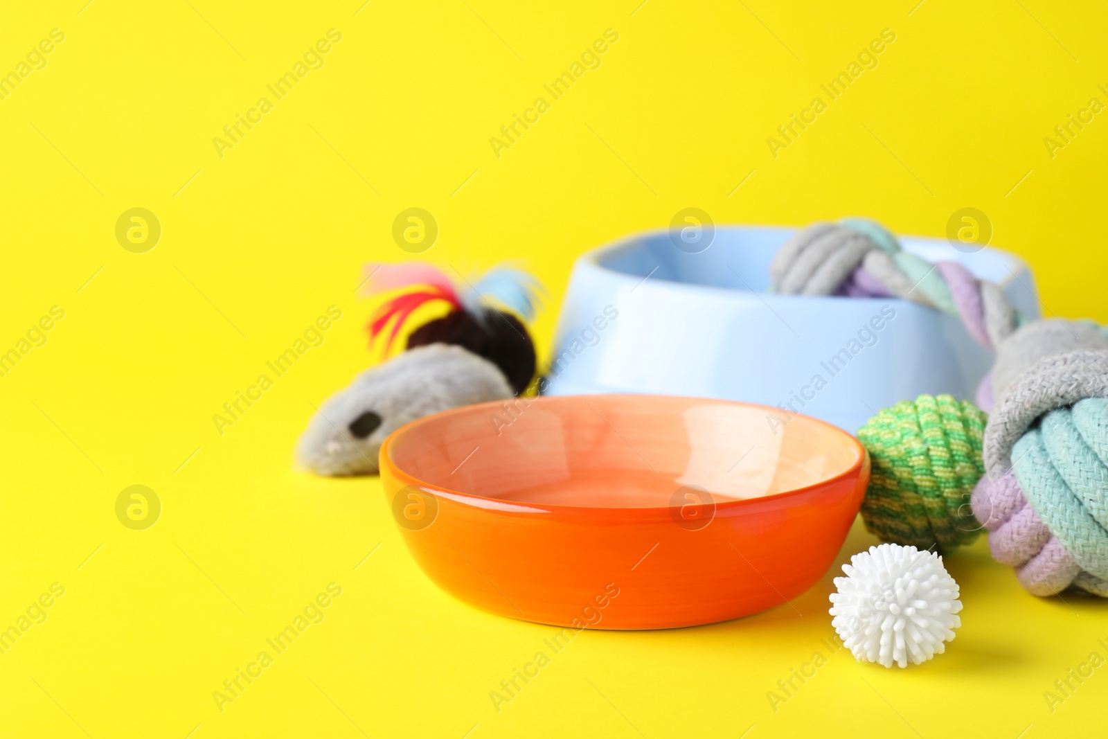 Photo of Feeding bowls and toys for pet on yellow background