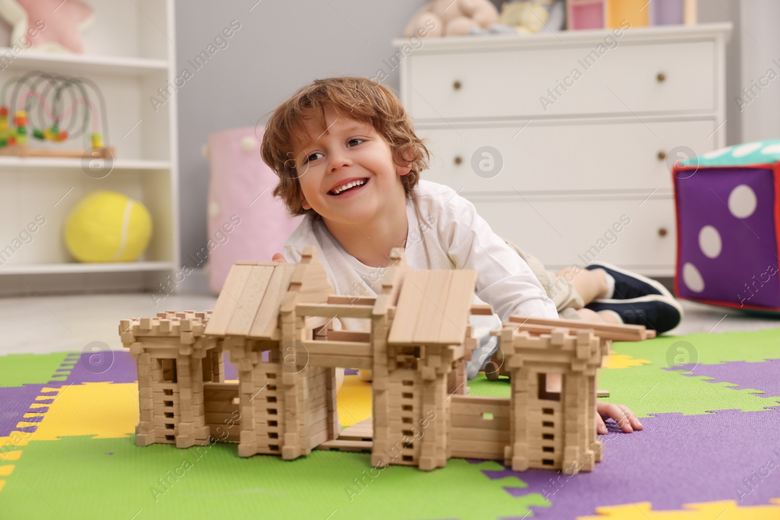 Photo of Little boy playing with wooden entry gate on puzzle mat in room. Child's toy