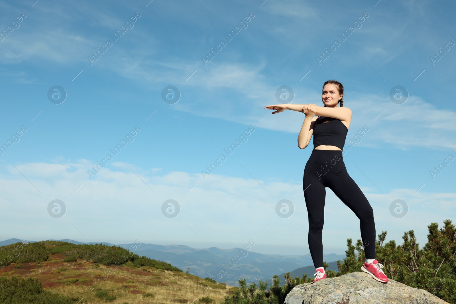 Photo of Beautiful young woman stretching on rock in mountains