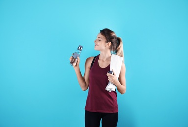 Photo of Beautiful young woman in sportswear with towel and bottle of water on color background