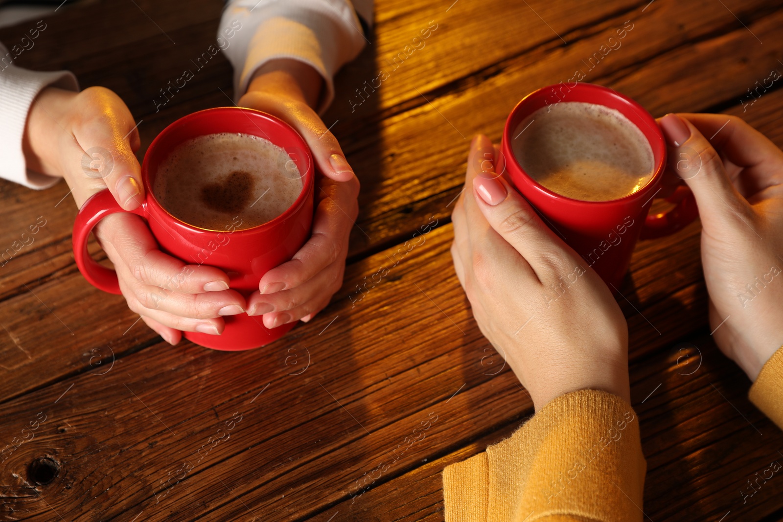 Photo of Women with mugs of hot coffee at wooden table, closeup