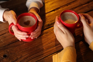 Women with mugs of hot coffee at wooden table, closeup