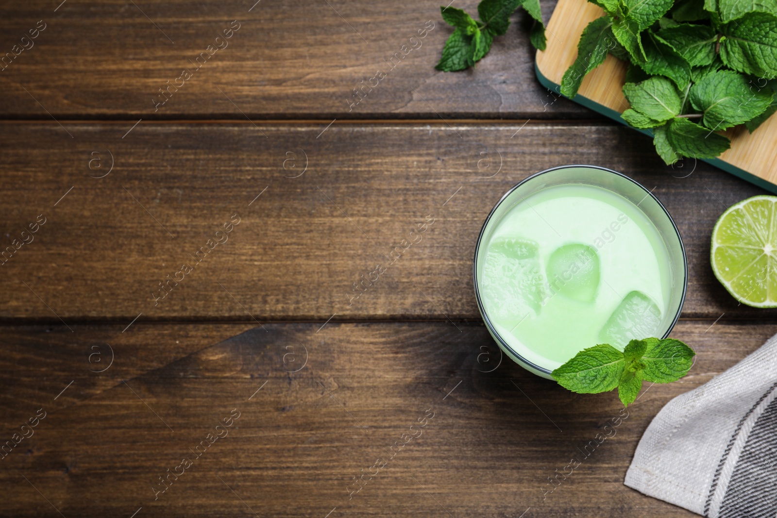 Photo of Delicious mint liqueur with green leaves and ice cubes on wooden table, flat lay. Space for text