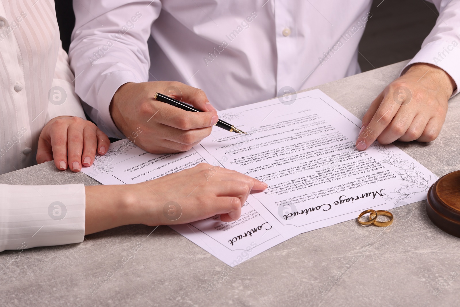 Photo of Man and woman signing marriage contract at light grey table, closeup