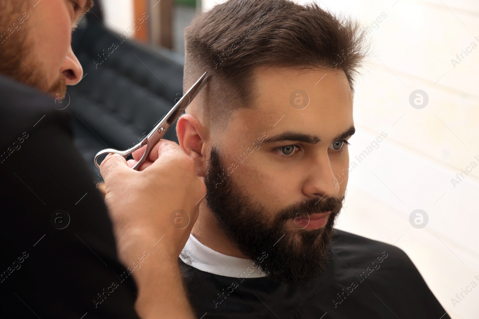 Photo of Professional hairdresser working with client in barbershop, closeup