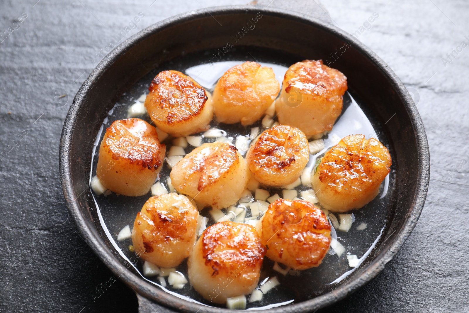 Photo of Delicious fried scallops in dish on dark gray textured table, above view