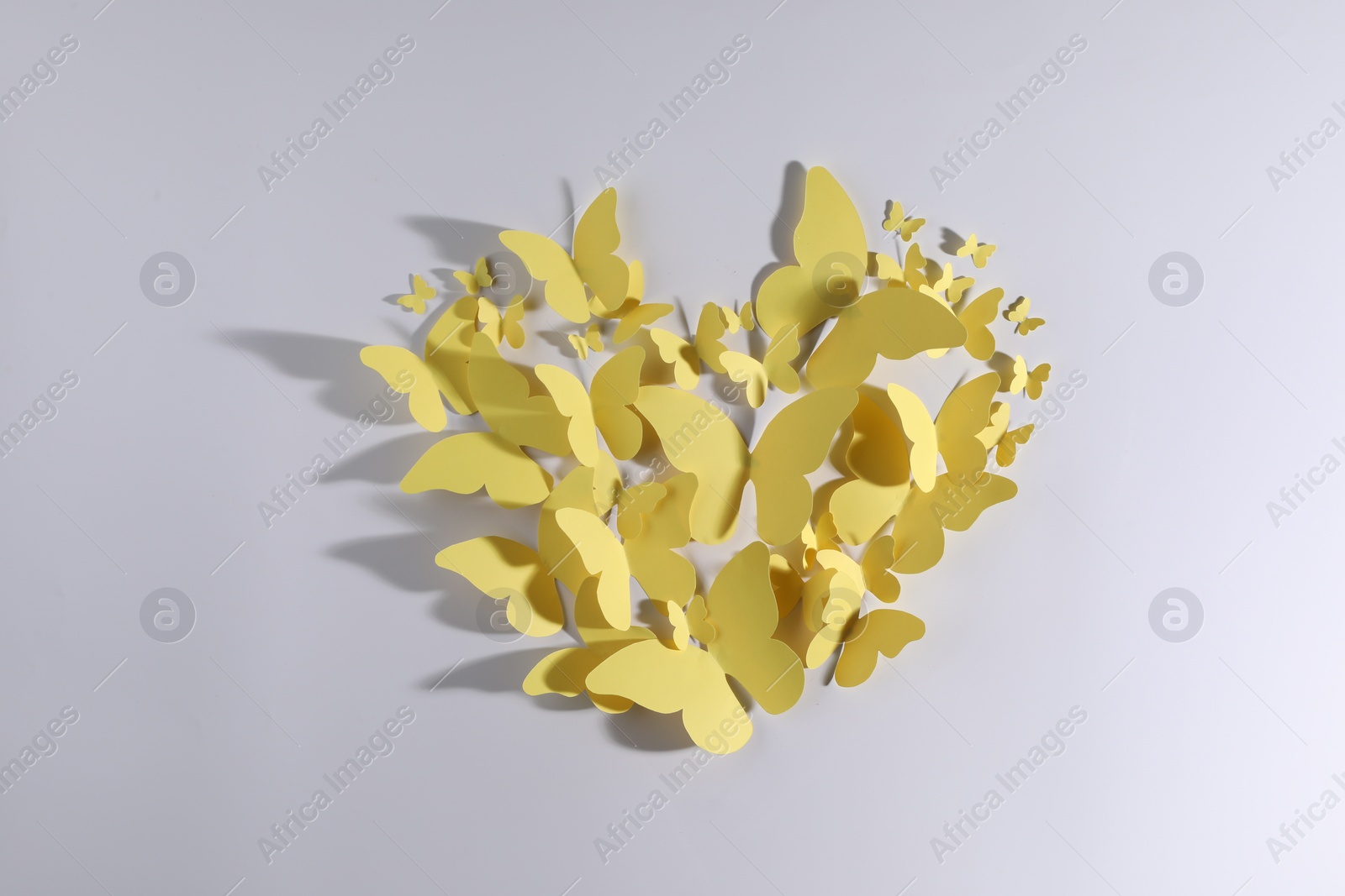 Photo of Heart shape made of yellow paper butterflies on white background, top view