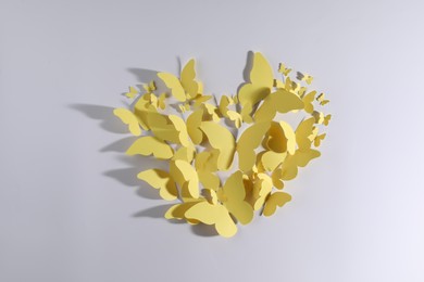 Photo of Heart shape made of yellow paper butterflies on white background, top view