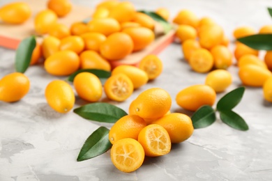 Photo of Fresh ripe kumquats and leaves on light grey table