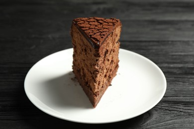 Photo of Piece of delicious chocolate truffle cake on black wooden table, closeup
