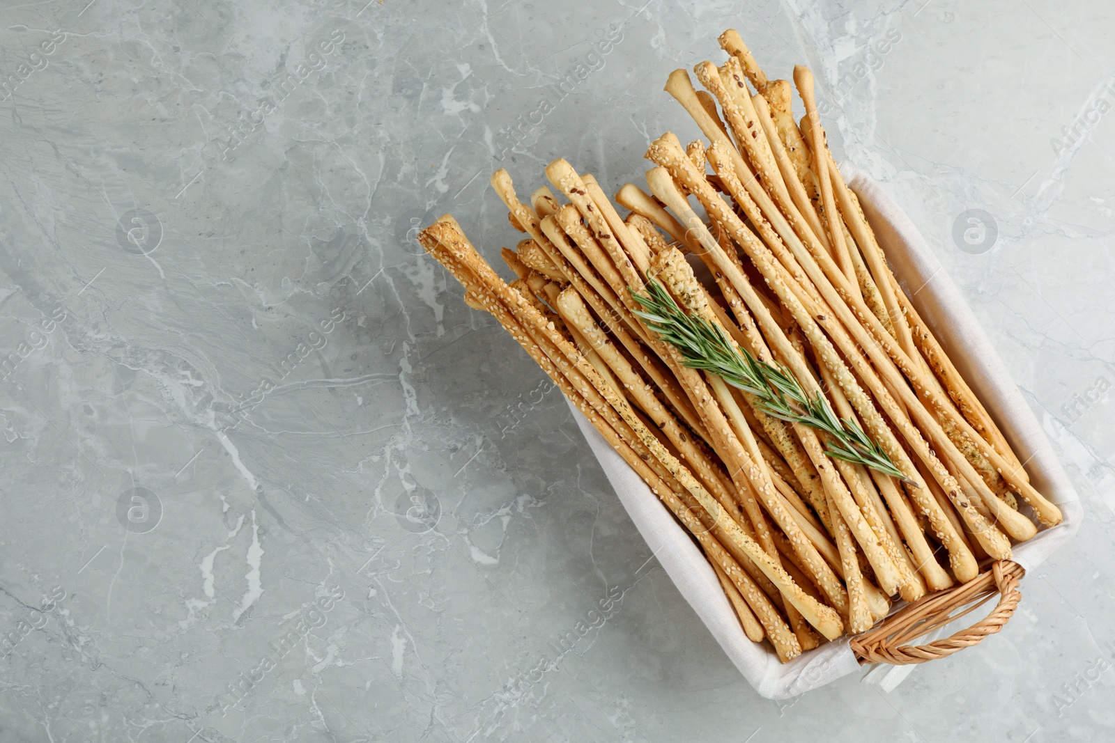 Photo of Delicious grissini sticks and rosemary on grey marble table, top view. Space for text