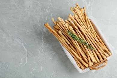 Photo of Delicious grissini sticks and rosemary on grey marble table, top view. Space for text