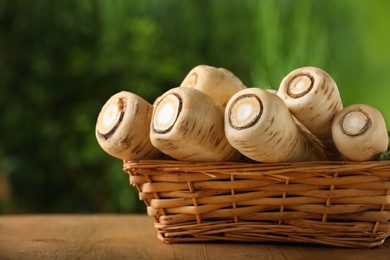 Photo of Wicker basket with delicious fresh ripe parsnips on wooden table outdoors