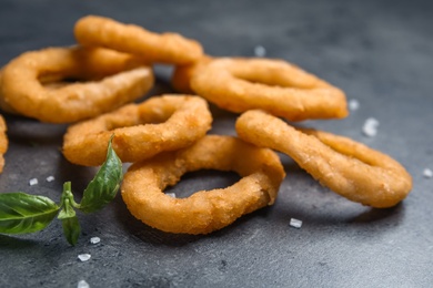 Photo of Fried onion rings and basil leaves on grey table