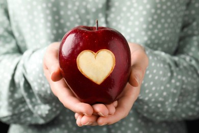 Woman holding red apple with carved heart, closeup