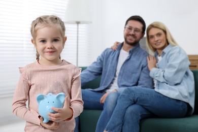Photo of Family budget. Little girl with piggy bank and her parents at home, selective focus