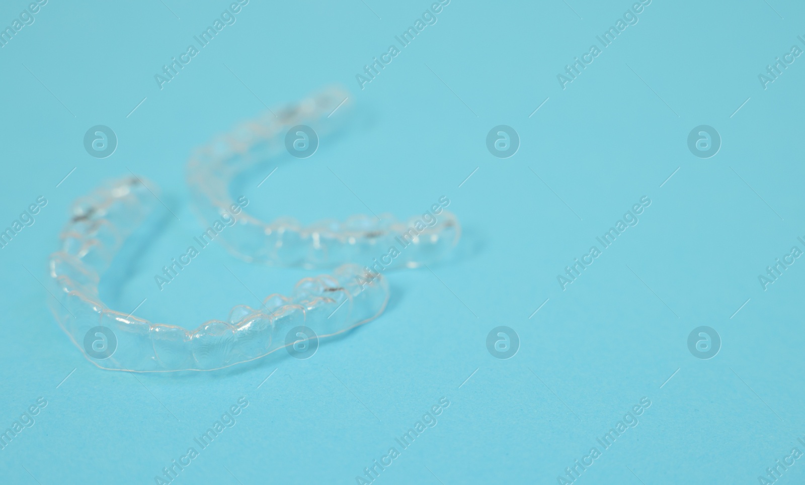 Photo of Transparent dental aligners on light blue background, closeup. Space for text