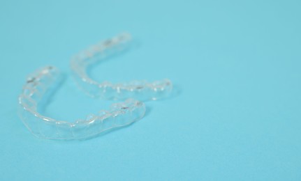 Photo of Transparent dental aligners on light blue background, closeup. Space for text