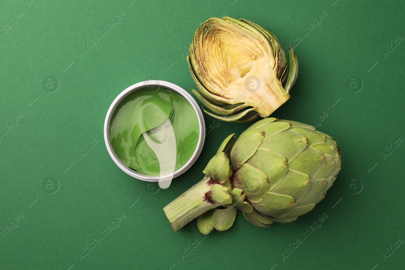 Photo of Package of under eye patches and artichokes on green background, flat lay. Cosmetic product