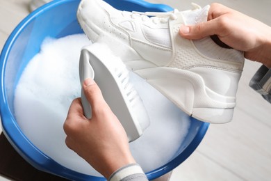 Woman cleaning stylish sneakers with brush in wash basin, top view