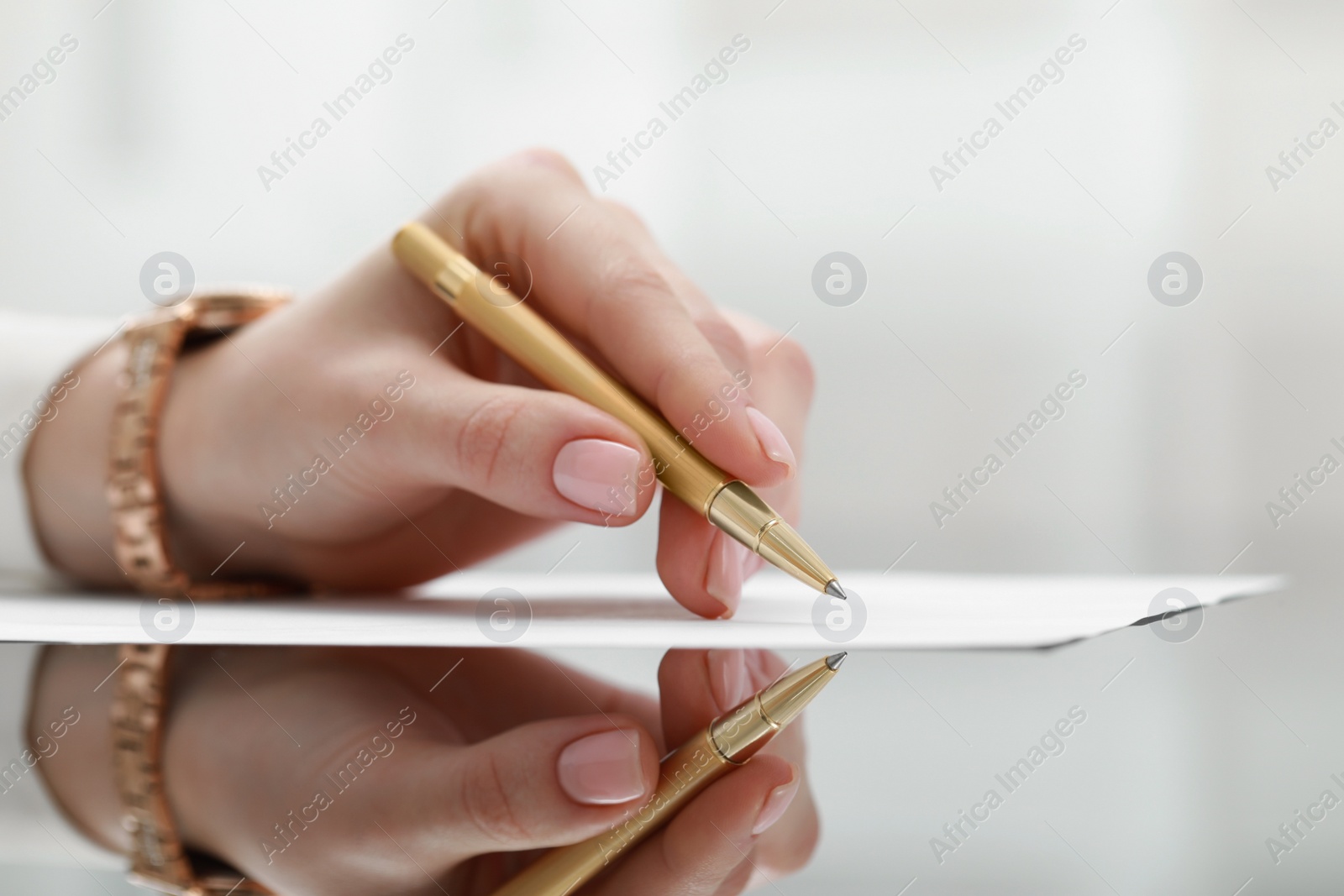 Photo of Woman writing on sheet of paper at glass table, closeup