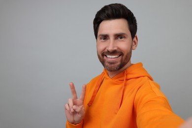 Photo of Smiling man taking selfie and showing peace sign on grey background, space for text