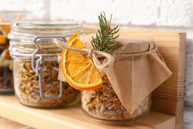 Photo of Jars of dried orange zest seasoning on wooden shelf near white brick wall