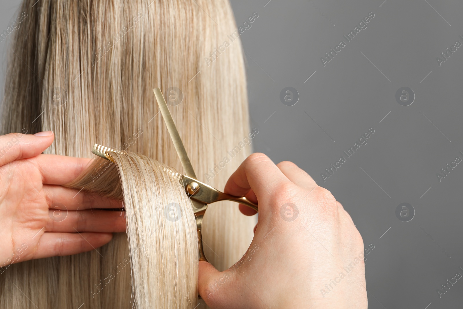 Photo of Hairdresser cutting client's hair with scissors on light grey background, closeup