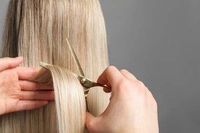 Photo of Hairdresser cutting client's hair with scissors on light grey background, closeup