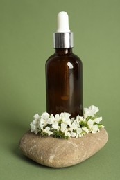 Composition with bottle of face serum, spa stone and beautiful flowers on light green background