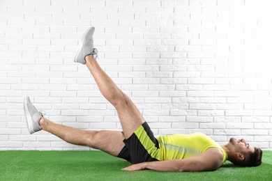 Photo of Handsome young man in sportswear doing scissors exercise on artificial green lawn near brick wall