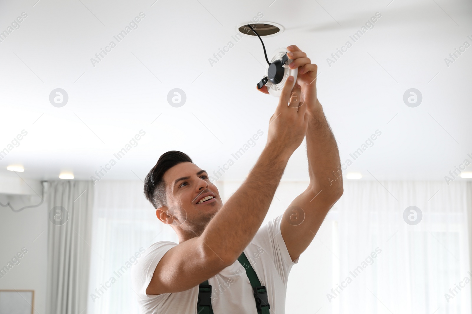 Photo of Electrician in uniform repairing lamp on ceiling indoors