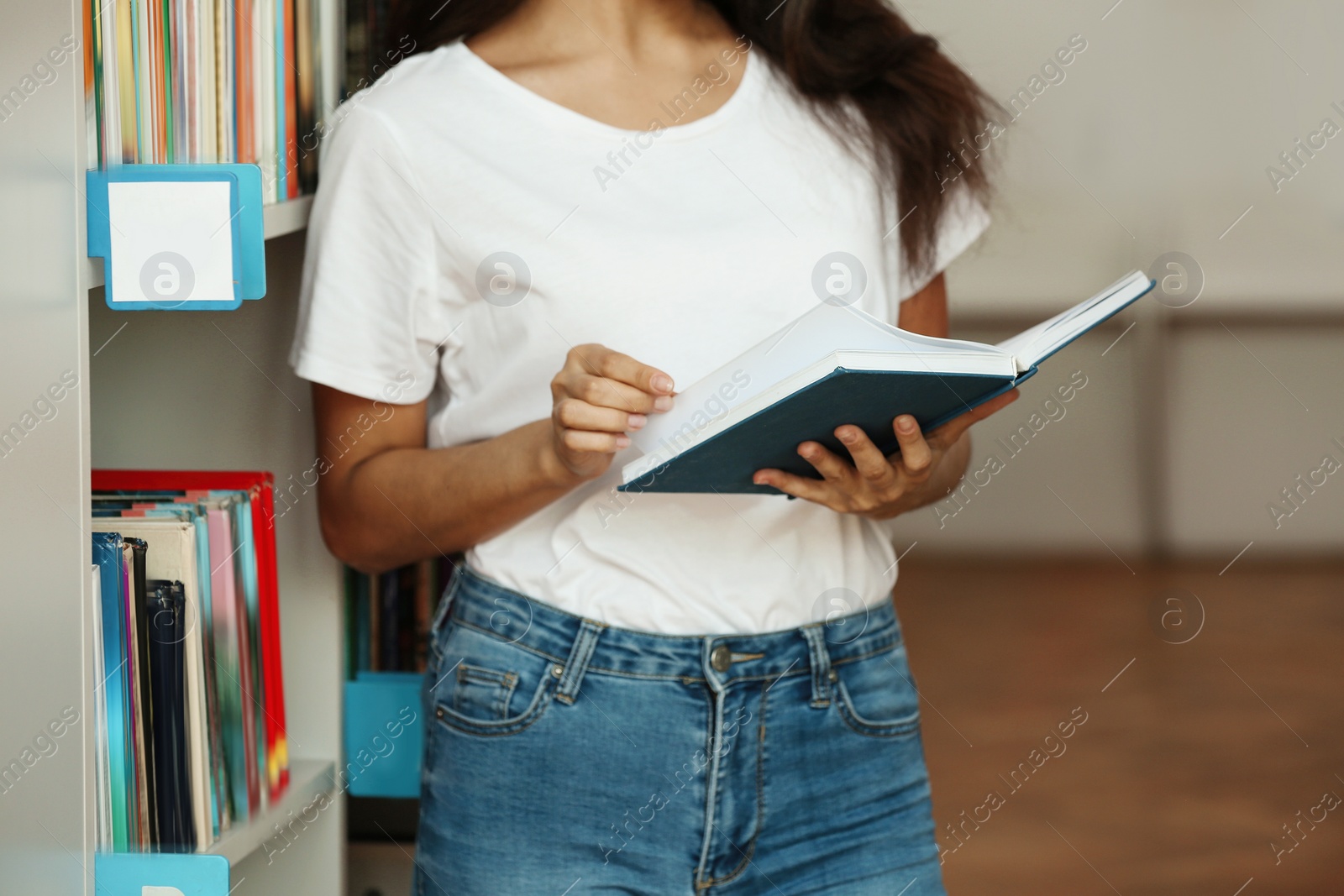 Photo of Young woman with book near shelving unit in library, closeup