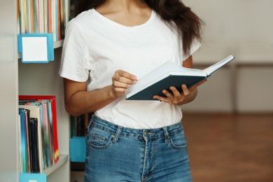 Photo of Young woman with book near shelving unit in library, closeup
