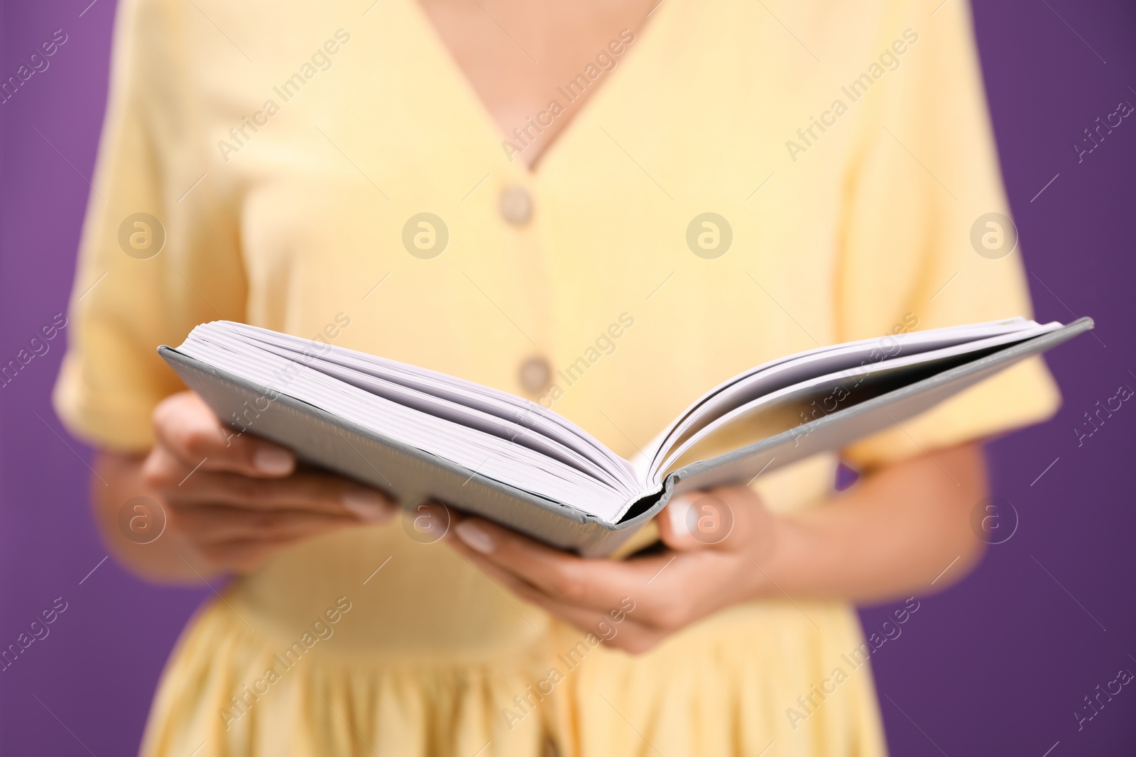 Photo of Young woman with book on purple background, closeup