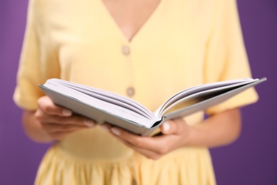 Young woman with book on purple background, closeup