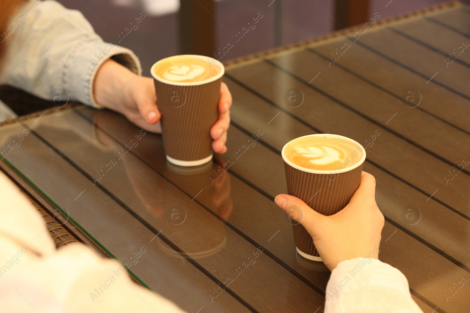 Photo of Women holding takeaway paper cups at table, closeup. Coffee to go