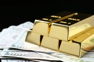 Photo of Shiny gold bars and money on black background, closeup