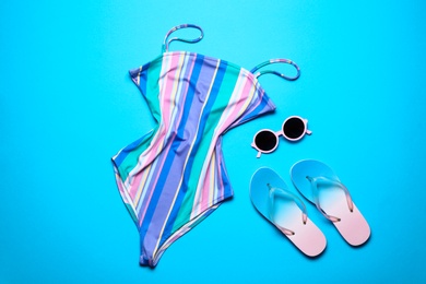 Photo of One-piece swimsuit, sunglasses and flip-flops on color background, top view